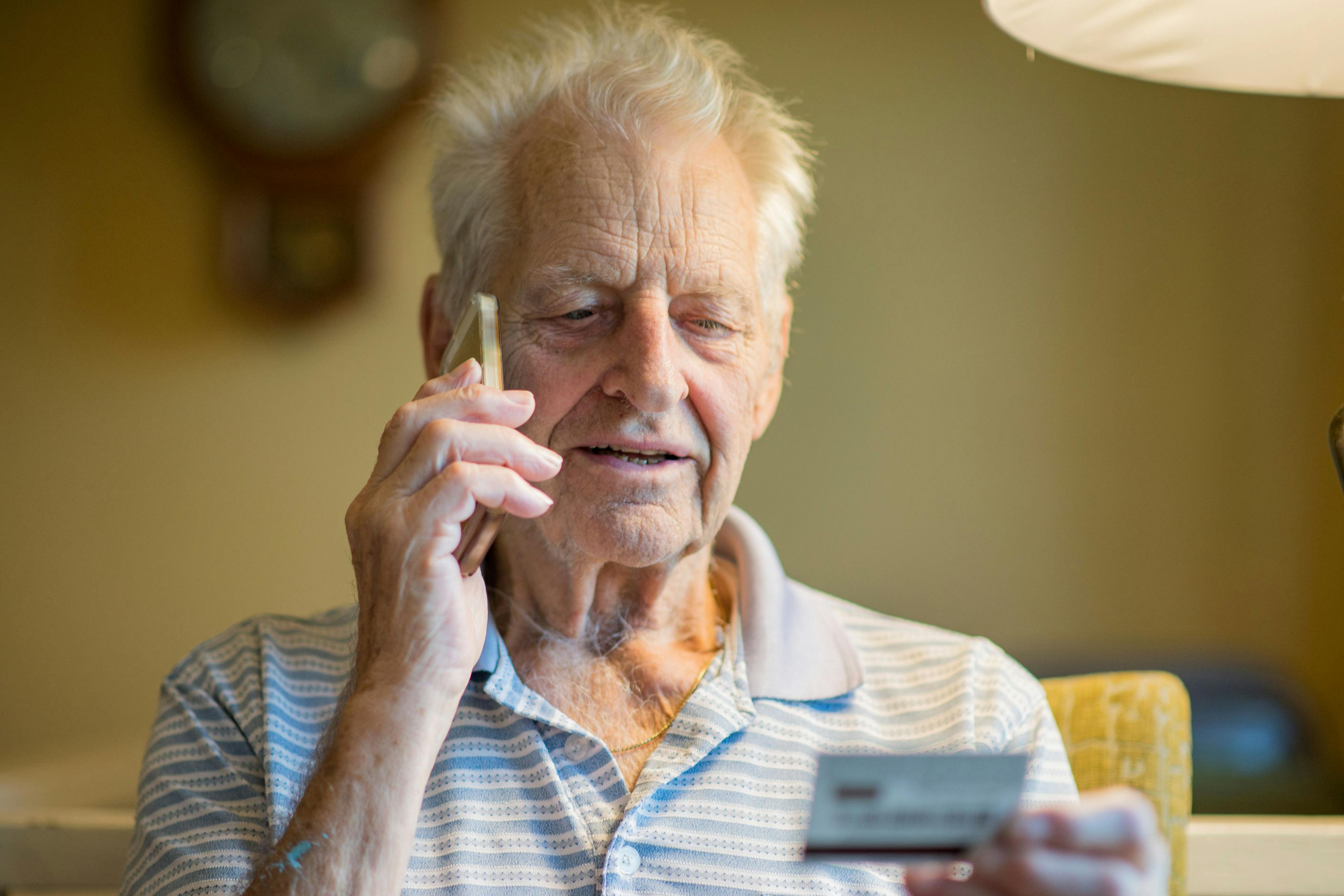 A white senior looks at his credit card information while on the phone.