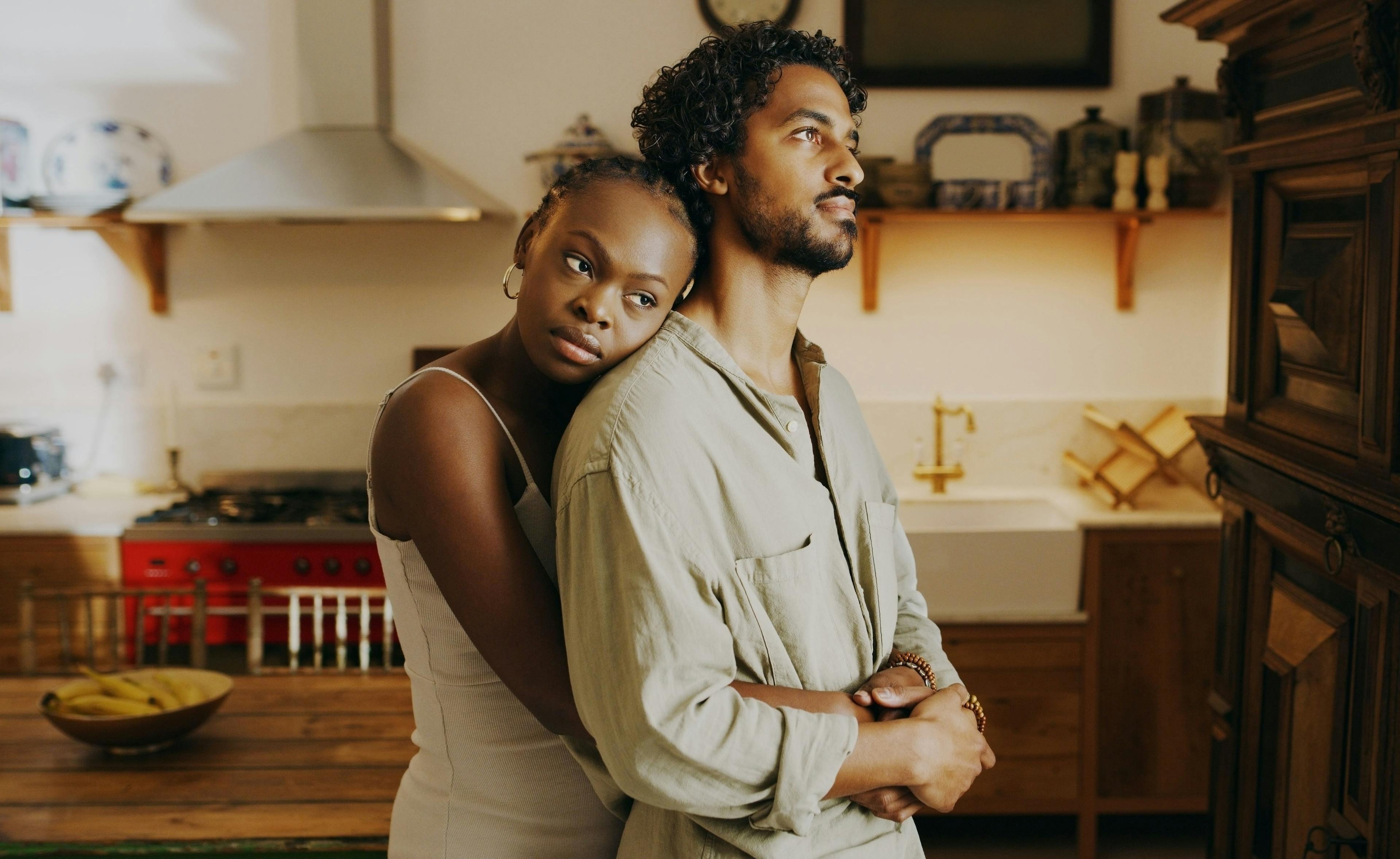 A Black couple hugs each other and stares out a window.