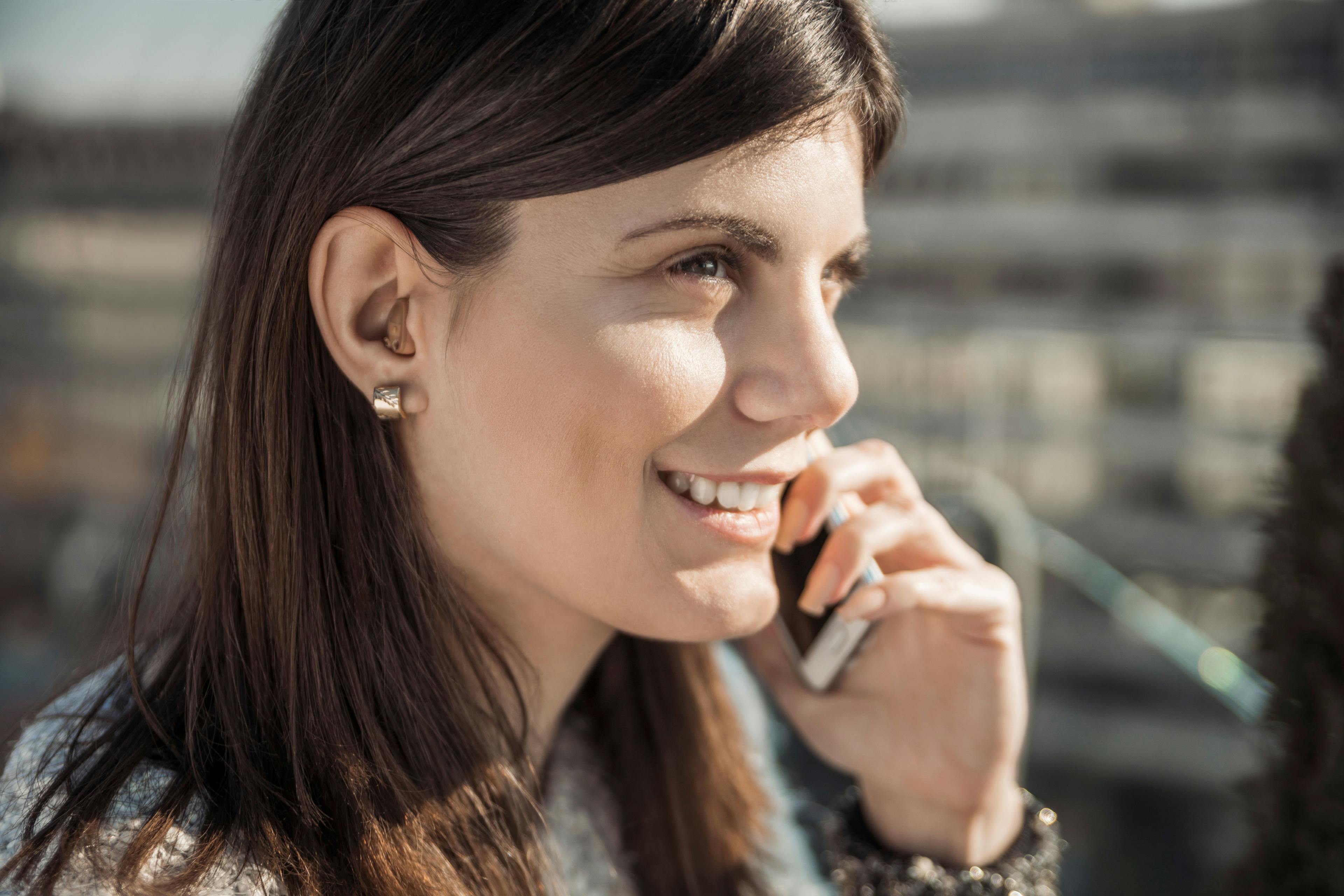 A smiling young woman with a hearing aid talks on the phone.