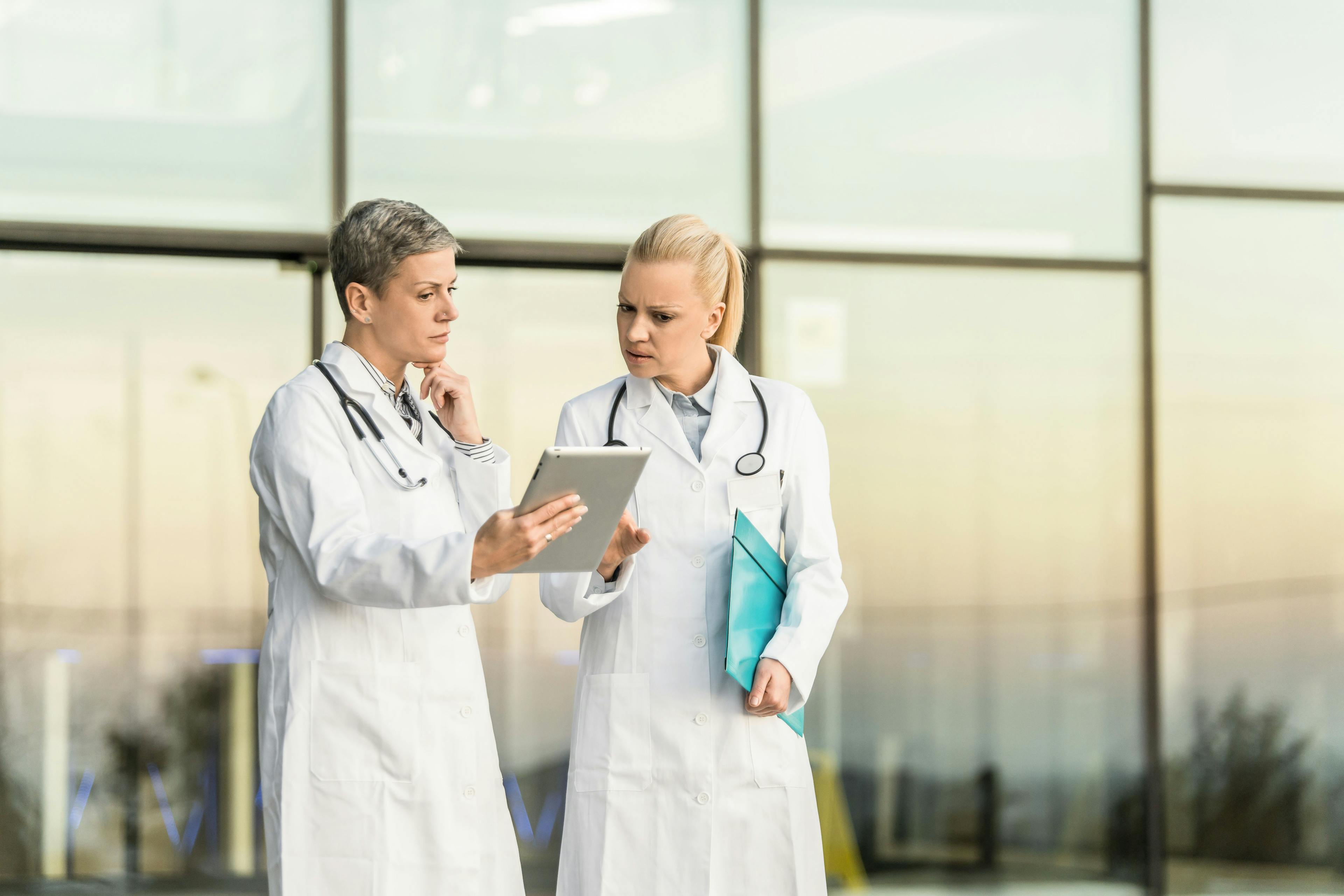Two worried female doctors hold a tablet.