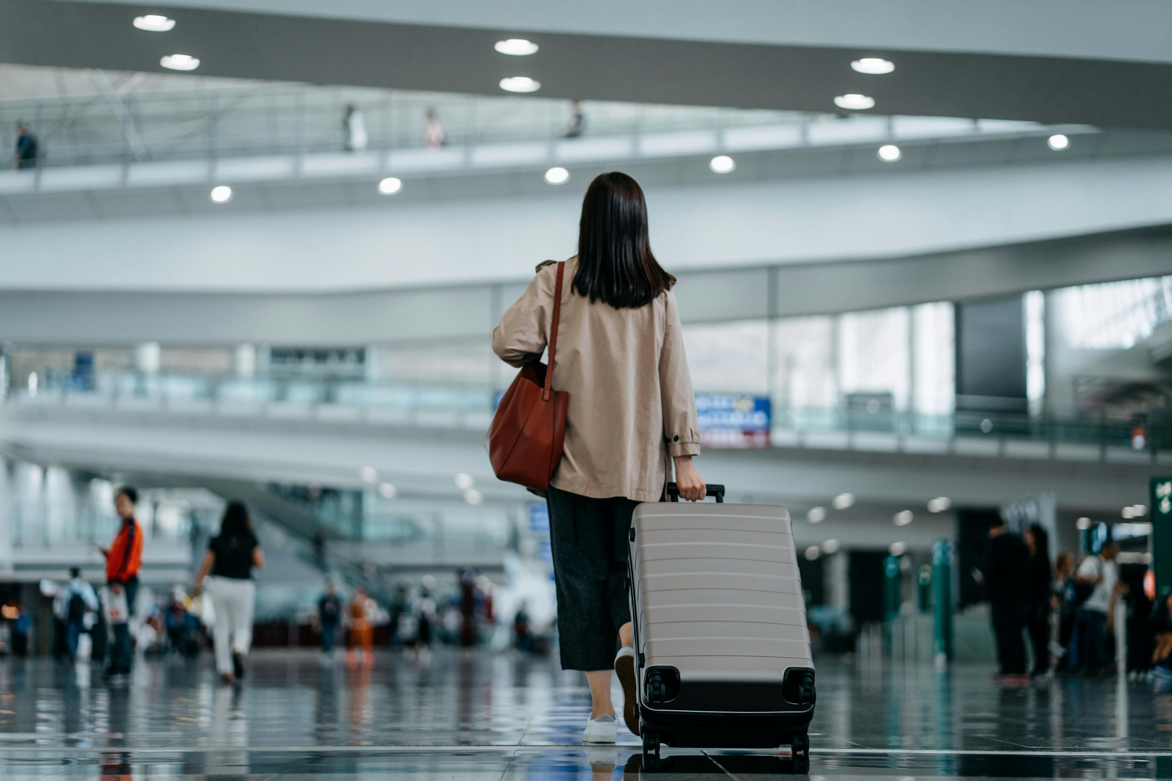 A woman walks away in an airport with luggage trailing behind her.