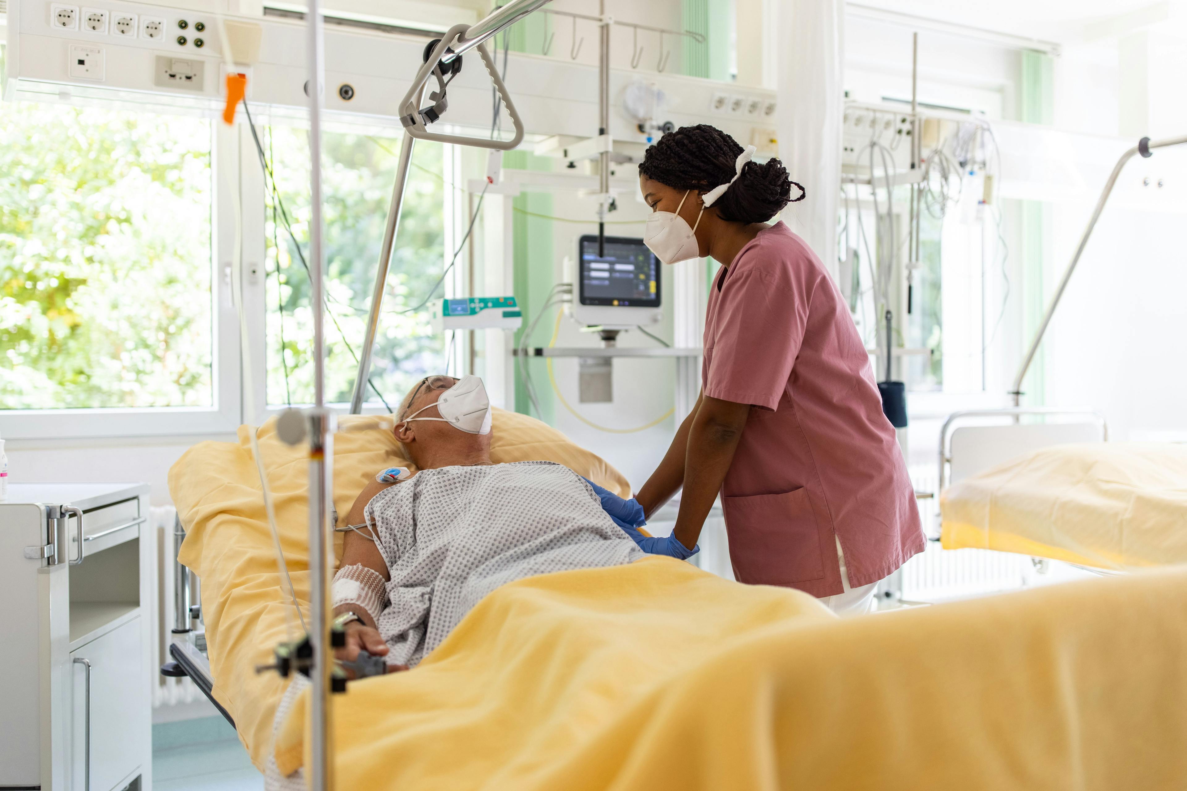 A Black nurse looks after an older patient in an ICU.
